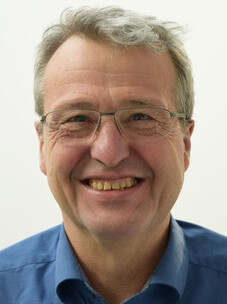 Porträt von Bernd Büchner mit Brille und breitem Lächeln vor hellem Hintergrund.